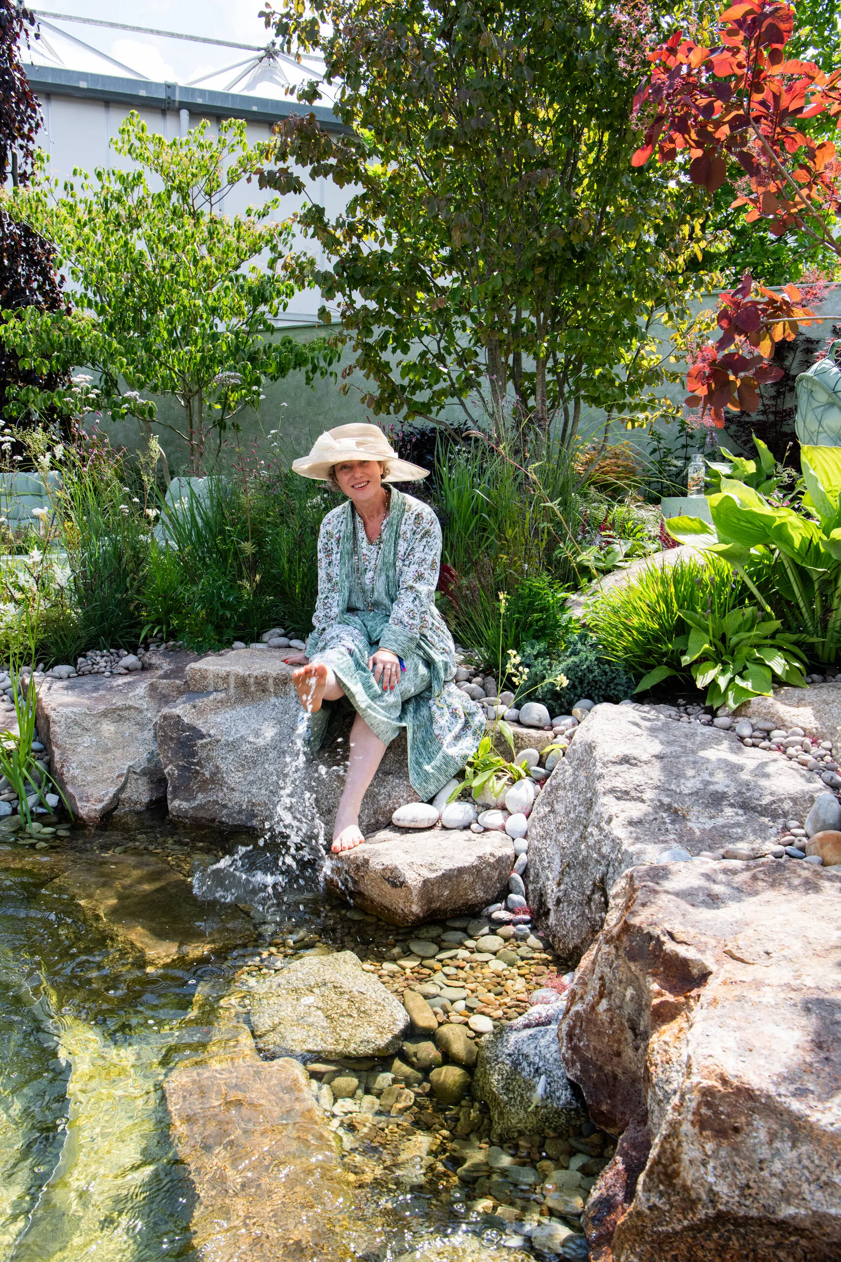 Garden designer Kitti Kovacs relaxing beside a naturalistic waterfall surrounded by lush planting