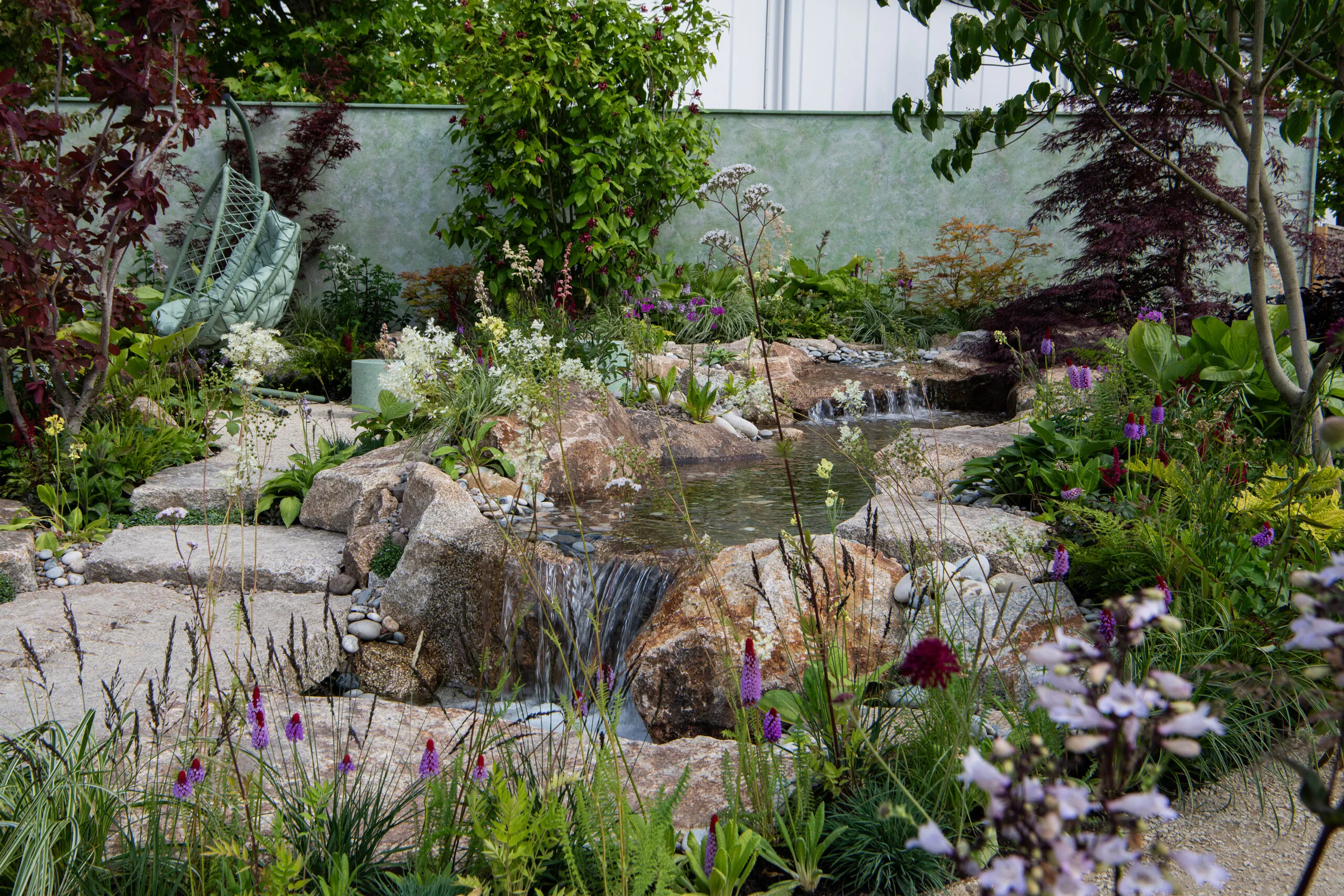 Naturalistic waterfall surrounded by lush perennial planting and granite boulders designed by Kitti Kovacs Garden Design