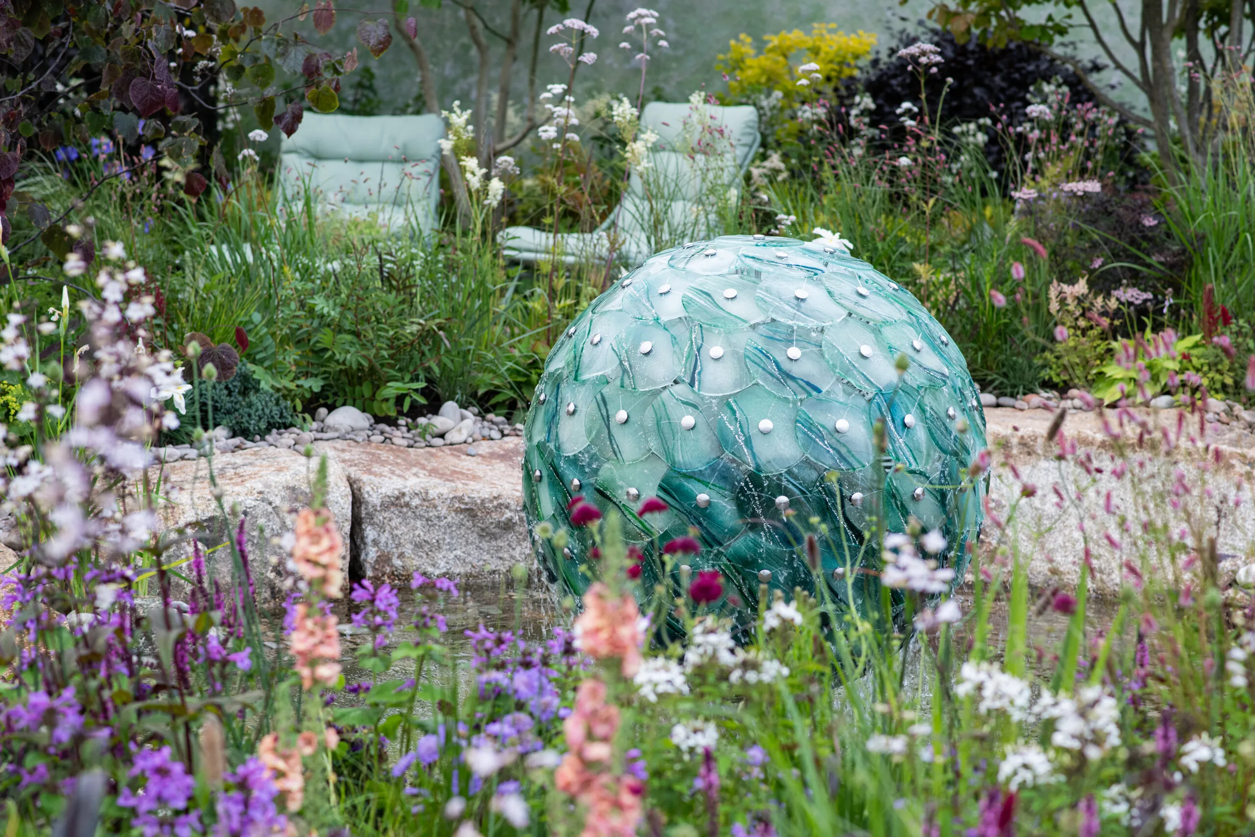 Sculptural glass water feature surrounded by colourful naturalistic planting in a contemporary garden